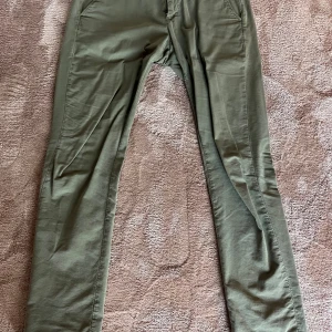 Olivgröna chinos från Dondup, strl 34 - Snygga olivgröna chinos från Dondup, tillverkade i Italien. Byxorna har en rak passform med klassiska fickor fram och bak, och är gjorda i ett mjukt bomullsmaterial med diskret struktur. Perfekt för dig som gillar stilrena och bekväma byxor.