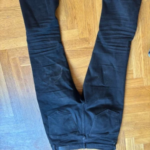 Svarta Perfect Jeans i storlek 36 - Svarta jeans från Perfect Jeans i storlek 36. Klassisk femficksmodell med raka ben och normal passform. Jeansen har svarta sömmar och diskreta nitar framtill. Perfekta för dig som gillar en enkel och stilren look.