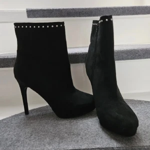 Svarta stövletter med nitar och klack - Snygga svarta stövletter i mocka-look med hög klack och rund tå. Dekorerade med små silverfärgade