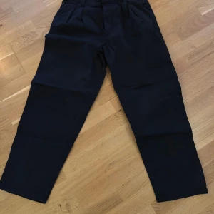 Svarta tapered kostymbyxor från BOSS - Svarta kostymbyxor från BOSS i modellen Tulsa Tapered Fit. Byxorna har avsmalnande ben, klassisk midja och pressveck framtill. Snygg och stilren look som passar perfekt till en dressad outfit. Materialet är mjukt och följsamt för extra komfort.