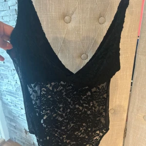 Svart spetsig linnetopp från Divided - Säljer en svart linnetopp från Divided i storlek M. Toppen är ärmlös och har djup v-ringning samt är helt täckt av spets med blommigt mönster. Perfekt att styla med jeans eller kjol för en trendig look.