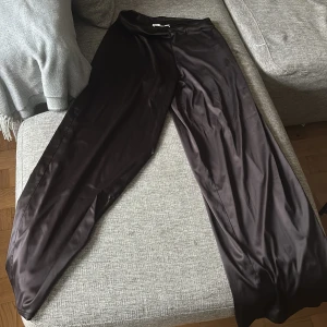 Svarta vida byxor i satin från Zara - Snygga svarta byxor från Zara i glansigt satinmaterial. De har en loose och wide passform med raka, långa ben och elastisk midja. Perfekta för dig som gillar en avslappnad men ändå trendig look.