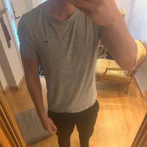 Grå t-shirt från Morris Stockholm - Snygg grå t-shirt från Morris  i mjuk bomull. Klassisk passform med rund hals och diskret broderad logga på bröstet. Perfekt basic-plagg som funkar till allt och är superenkel att matcha med jeans eller shorts.