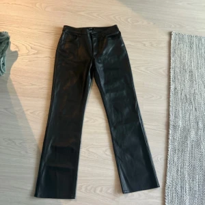Svarta skinnbyxor från BikBok - Svarta byxor i skinnimitation från BikBok med raka ben och klassisk femficksdesign. Byxorna har bälteshällor och knappstängning framtill. Snyggt stilrena och passar perfekt till en trendig look. Helt oanvänd 