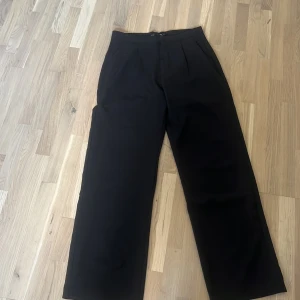 Svarta kostymbyxor från 157 - Svarta kostymbyxor från 157 i storlek S. Byxorna har en rak och lite vidare passform med klassisk midja och pressveck framtill. Perfekt för en clean och stilren look. Materialet känns mjukt och har en lätt struktur.