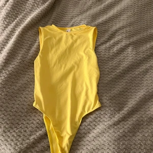 Gul ärmlös bodysuit från Missguided - Säljer en solgul bodysuit från SHEIN i storlek S. Bodyn är ärmlös🥰