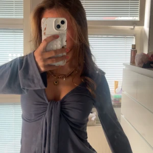 Mörkgrå topp från Gina Tricot - Supersnygg mörkgrå omlottopp från Gina Tricot med långa ärmar och djup v-ringning. Toppen har knyt framtill som ger en cool och trendig look. Perfekt att styla med jeans eller kjol för en chic vibe.