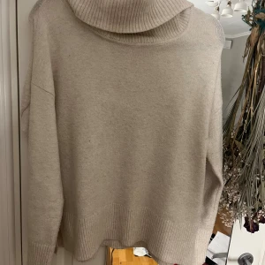 Beige polotröja från Vero Moda - Beige polotröja från Vero Moda i storlek S. Tröjan har en bred, ribbad polokrage och ribbade muddar vid ärmslut och nederkant. Den är stickad och har en loose passform med långa ärmar.