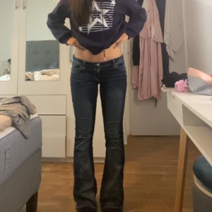 Mörkblå bootcut jeans med broderi - Säljer ett par mörkblå bootcut jeans med snygga broderade detaljer på bakfickorna. Jeansen har låg midja och klassisk femficksdesign. Materialet är stretchigt jeans och passformen är slim upptill med utsvängda ben. Perfekta för dig som gillar en cool och trendig look.