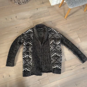 Svartvit kofta med mönster - Säljer en svartvit kofta i storlek S. Koftan har ett fett grafiskt mönster i vitt och svart, bred krage och är stickad i mjukt material. Perfekt att slänga på sig när det är lite kyligt ute. Långärmad och loose fit för chill vibe.