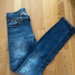 Blå slim jeans från Nudie Jeans - Säljer ett par blå slim jeans från Nudie Jeans i storlek W25 L32. Jeansen har klassisk femficksdesign, orangea sömmar och snygga detaljer på bakfickorna. De är tillverkade i stretchigt denim passform och har en något ljusare tvätt på låren.
