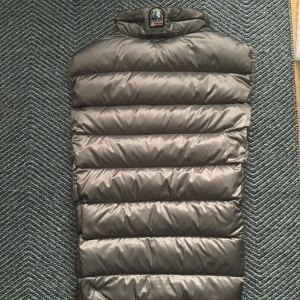 Mörkgrön  dunväst från Parajumpers - Snygg mörk grön dunväst från Parajumpers med orange foder. Västen har hög krage, dragkedja framtill och två fickor med dragkedja. Quiltad design med breda kanaler och märkets logga på kragen. Perfekt för lager-på-lager under kyliga dagar. Knappast använd och är i perfekt skick. Sizen är Young Large och passar perfekt nu för hösten. OBS inget kvitto på varan. Nypris: 4000kr