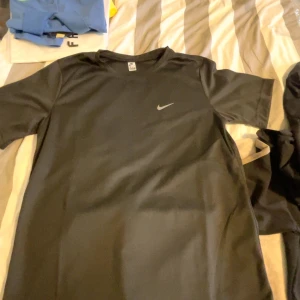 Svart Nike Dri-Fit t-shirt 3XL - Svart t-shirt från Nike i storlek 3XL med Dri-Fit-teknologi. Klassisk passform med korta ärmar och rund hals. Perfekt för träning med sitt lätta och snabbtorkande material. Diskret Nike-logga på bröstet för en clean sportig look.