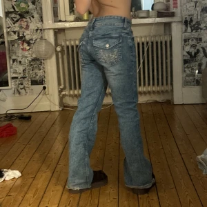 Blå bootcut jeans med broderad ficka - Säljer ett par ljusblå bootcut jeans med snygg broderad detalj på bakfickan. säljer pga de är lite stora för mig i midjan, jag har klippt dem längst ner så de passar korta människor, 150-155cm