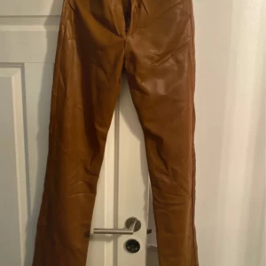 Bruna skinnbyxor med raka ben - Snygga bruna byxor i skinnimitation med raka ben och klassisk femficksmodell. Byxorna har hög midja och stängs med knapp och dragkedja. Perfekta för dig som vill sticka ut med en cool och trendig look.