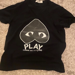 Svart Comme des Garçons Play t-shirt - Svart t-shirt från Comme des Garçons Play med stort vitt hjärta med ögon och logga på bröstet. Klassisk rund hals och korta ärmar. Skön passform och tillverkad i mjuk bomull. Perfekt statement-plagg för dig som gillar streetstyle.
