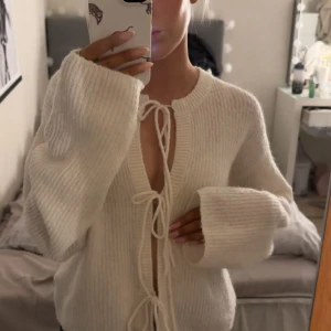 Vit stickad kofta från Gina Tricot XS - Supermysig vit stickad kofta från Gina Tricot i ullblandning. Koftan har långa, vida ärmar och snygga knytband framtill. Perfekt för lager på lager och chill vibes. Passar dig som gillar en loose och avslappnad stil.