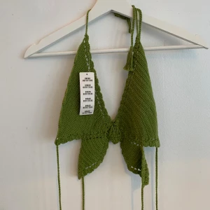 Olivgrön virkad topp Urban Outfitters - Superfin olivgrön virkad topp från Urban Outfitters i 100% bomull. Triangelformad modell med knyt i nacken och ryggen, samt snygga virkade detaljer. Perfekt för strandhäng, festival eller sommarvibbar! Aldrig använd