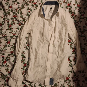 Vit slim fit skjorta från G-Star RAW stl XS - Säljer en vit skjorta från G-Star RAW i slim fit-modell. Skjortan har klassisk krage med blå insida, långa ärmar och knappar vid manschetterna. Tillverkad i bomull och passar perfekt till dig som gillar en clean och stilren look. Stl XS