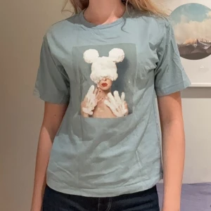 Söt T-shirt - Säljer en ljusblå t-shirt med ett stort konstnärligt tryck framtill som föreställer en person med vita handskar och musöron. T-shirten har klassisk passform och korta ärmar. Perfekt för dig som gillar unika motiv och chill stil. Aldrig använd!