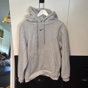 Nike hoodie - Säljer en grå hoodie från Nike i storlek L. Tröjan har en klassisk huva med snörning, magficka och mjukt fleecefoder på insidan. Perfekt för chill dagar eller när du vill ha något bekvämt och stilrent. Diskret Nike-logga broderad på bröstet. Aldrig använd.