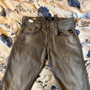 Replay Anbass grå slim fit jeans 29/32 - Snygga grå Replay Anbass jeans i slim fit med klassisk femficksdesign. Jeansen har normal midja och är tillverkade i ett mjukt bomullsmaterial med stretch för extra komfort. Perfekta för dig som gillar stilrena och laidback jeans.