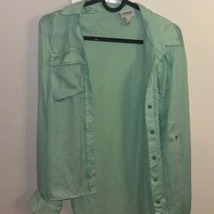 Mintgrön skjorta från Vero Moda Aware XS - Snygg mintgrön skjorta från Vero Moda Aware i tunn och lätt bomull. Skjortan har klassisk krage, långa ärmar och knäppning framtill.