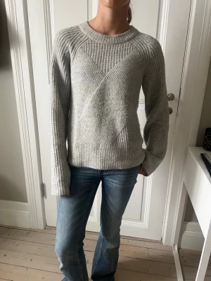 Ljusgrå stickad tröja med struktur - Säljer en ljusgrå stickad tröja med snygg struktur och diskreta ränder. Tröjan har rund halsringning och långa ärmar. Perfekt till jeans för en chill och stilren look.