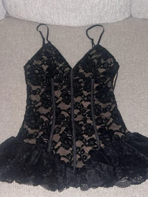 Svart spetstopp - Säljer en svart spetsväst från Zara i storlek S. Toppen har tunna axelband, v-ringad hals och är dekorerad med blommig spets och volangkant nedtill. Helt oanvänd och prislappen sitter kvar, säljer pga storleken