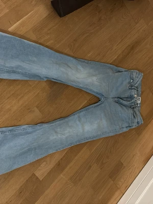 Ljusblå bootcut jeans - Säljer ett par ljusblå jeans med bootcut-modell. Jeansen har klassisk femficksdesign, normal passform och är tillverkade i jeansmaterial. Perfekta för dig som gillar retrovibbar och vill ha ett par snygga utsvängda byxor liten fläck men går att gömma med en cardigan .