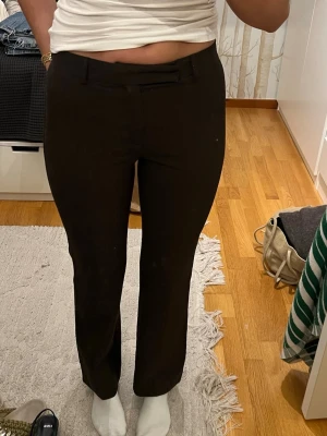 Bruna kostymbyxor från Zara Woman - Säljer ett par bruna kostymbyxor från Zara Woman i storlek 36. Byxorna har hög midja, utsvängda ben och bälteshällor. Materialet är en mix av polyester, rayon och spandex vilket gör dem både bekväma och stretchiga. Perfekta till en snygg och clean look. Säljer då de tyvärr är för korta för mig!