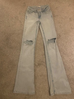 Bootcut jeans med slitna knän från Nelly - Ljusblå bootcut jeans från Nelly med slitna hål på båda knäna och ett snyggt rosa mönster på bakfickorna⭐️. Används ett par gånger så inte helt nya.💋 Nyttpris 699kr och pris kan diskuteras🫰🏻