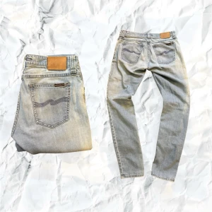 Ljusblå jeans från Nudie Jeans, W30 L32 - Säljer ett par ljusblå jeans från Nudie Jeans med klassisk femficksdesign och snygga kontrastsömmar. Jeansen har en rak passform och är tillverkade i mjukt bomullsmaterial. Bakfickorna har Nudie Jeans ikoniska broderade vågmönster. Våga ställa frågor och kan diskutera pris vid snabb affär.