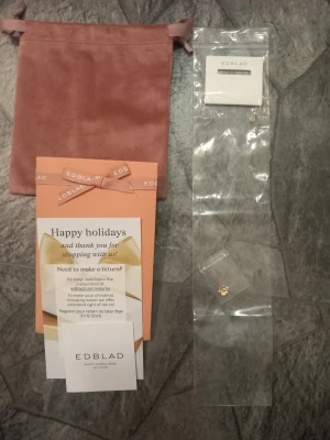 Ett blommhalsband  -  Ett guld halsband från Edblad med blomma som design, samt tillhörande förpackning och jättefin rosa påse. Aldrig andvänd.