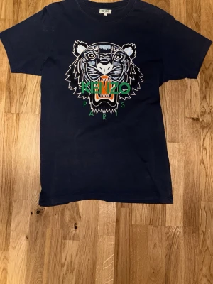 Mörkblå Kenzo t-shirt med tigertryck - Snygg mörkblå t-shirt från Kenzo i bomull med ikoniskt tigertryck och grönt Kenzo Paris-tryck på bröstet. Klassisk passform och korta ärmar.