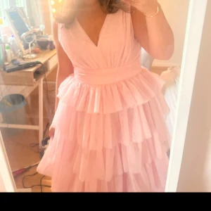 Ljusrosa balklänning från bubbleroom  - Supersöt ljusrosa balklänning med flera lager volanger och v-ringad hals. Materialet känns lätt och luftigt. Klänningen är i storlek 40 men jag som är 158 har sytt upp den både i axelbandet och på längden. Den är liten i storlek så jag som annars har 38 fick ta större storlek. Som nu kostar den 1800 där av priset 