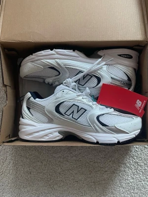 Vita New Balance 530 sneakers - Säljer ett par fräscha New Balance 530 sneakers i vitt med detaljer i silver och svart. Skorna har meshpaneler för extra andningsförmåga, klassisk snörning och en chunky sula i gummi. Perfekta för dig som gillar sportig och clean stil. Tveka inte att höra av dig vid några frågor eller funderingar🤗