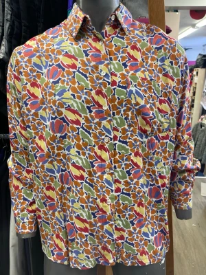 Färgglad blommig skjorta i bomull - Säljer en skjorta med färgstarkt blommigt mönster i orange, blått, grönt, rött och gult. Skjortan har klassisk krage, knäppning framtill och långa ärmar. Materialet är mjuk bomull som känns skönt mot huden. Perfekt för dig som vill sticka ut med en unik look.