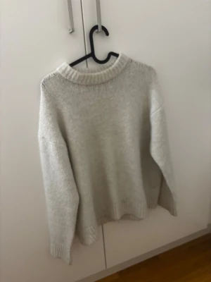 Ljusgrå stickad tröja med rund hals - Mysig ljusgrå stickad tröja med rund halsringning och ribbade muddar. Perfekt för kyliga dagar och enkel att matcha med jeans eller kjol. Tröjan har en loose passform och långa ärmar för extra komfort.