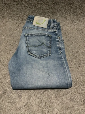 Jacob Cohen - Snygga ljusblå jeans från jacob Cohen med grön broderad detalj på bakfickan och patch med grön J på linningen. Klassisk femficksmodell i mjukt denimtyg, perfekt för en avslappnad look. Mer bilder så är det bara att skriva W33 103CM L W 38cm
