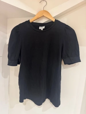 Svart topp från Aware by Vero Moda - En svart topp från Aware by Vero Moda med puffiga korta ärmar och rund halsringning. Tillverkad i mjuk bomull som känns skön mot huden. Enkel och stilren design som passar till många olika looks.