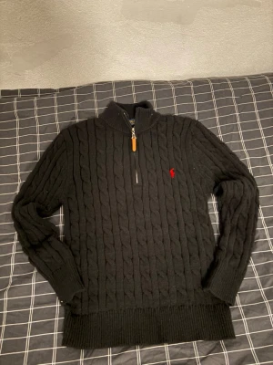 Svart stickad half zip från Polo Ralph Lauren - Säljer en svart stickad tröja från Polo Ralph Lauren med half zip och det klassiska röda logobroderiet på bröstet. Tröjan har lång ärm, ribbade muddar och en hög krage. Perfekt för dig som gillar stilren och tidlös design. Bara testad på annars i nyskick. Hör av dig om du har några frågor.