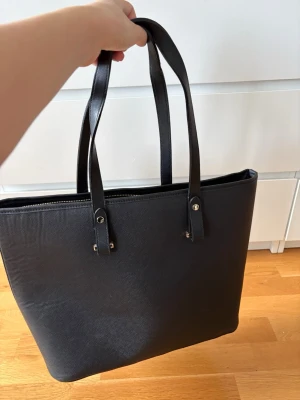 Svart väska - Säljer denna svarta väskan från hm med guldiga detaljer. Alla kedjor fungerar. Finns tre olika innerfack och är i fint skick. Normalstor handväska. Perfekt till skola, arbete eller shopping. Skriv om du har frågor!