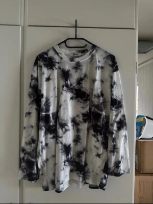 Svartvit tie-dye långärmad tröja - Säljer en långärmad tröja från YesStyle i svartvitt tie-dye mönster. Tröjan har en avslappnad passform och rund halsringning. Perfekt för dig som gillar streetwear och vill ha en unik look.