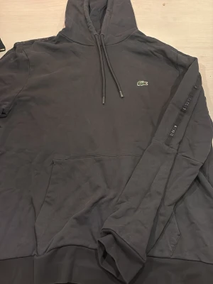 Lacoste hoodie - Grå Lacoste hoodie med svart Lacoste rand på armarna