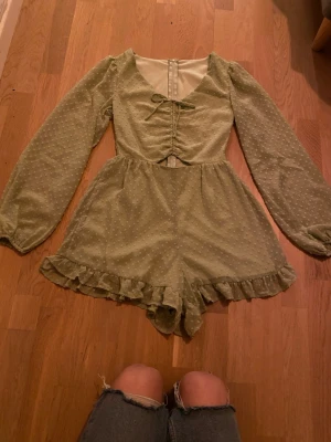 Grön byxdress med volang från FB Sister  - Supersöt ljusgrön byxdress från FB Sister i storlek XXS. Prickigt mönster, långa ärmar och volangkant nertill. Byxdressen har snörning framtill och dragkedja i ryggen. Vill siga att den är som xs i storlek om inte s .