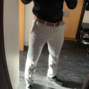 Ljusgrå kostymbyxor i rak modell från Dressman - Säljer ett par ljusgrå kostymbyxor med klassisk rak passform och pressveck. Byxorna har bälteshällor och stängs med dragkedja och knapp. Perfekta för en clean och stilren look, passar till skjorta eller t-shirt. Nypris 800kr, mitt pris 150kr. Storlek på dem är 31/32