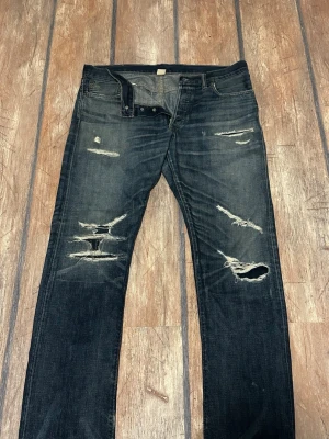 Double RL slitna blå jeans 34x34 - Säljer ett par blåa jeans från Double RL i storlek 34x34. Jeansen har flera slitningar och hål för en riktigt rå och trendig look. Tillverkade i 100% bomull och har klassisk femficksdesign. Perfekta för dig som gillar en edgy streetstil.