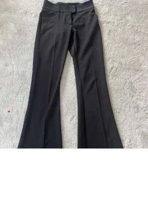 Svarta bootcut kostymbyxor - Snygga svarta kostymbyxor med bootcut passform och hög midja. Byxorna har en stilren look med pressveck och en enkel bakficka. Perfekta till en trendig outfit och passar till många olika stilar. 