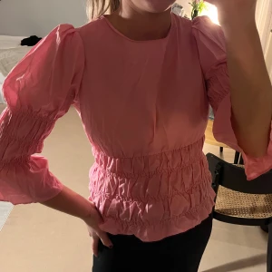 Rosa blus från Visual Clothing Project - Supersöt rosa blus med puffiga trekvartsärmar och smockdetaljer i midjan och på ärmarna. Storlek xs, i mycket bra skick!
